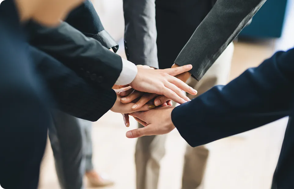 ビジネスシーンで複数人が手を重ね、チームで協力する姿